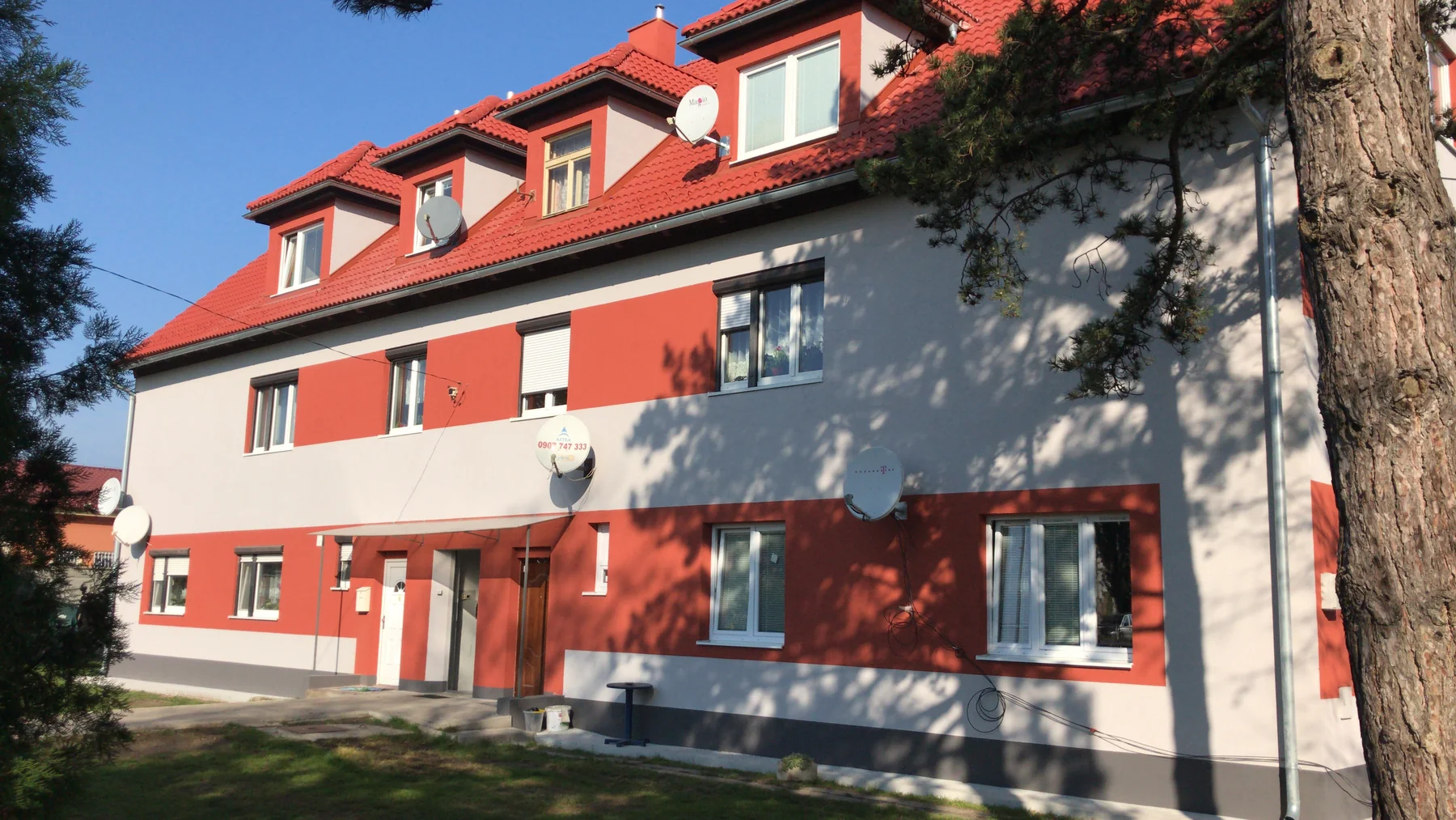 Bytový dom s bielou a červenou fasádou a červenou strešnou krytinou