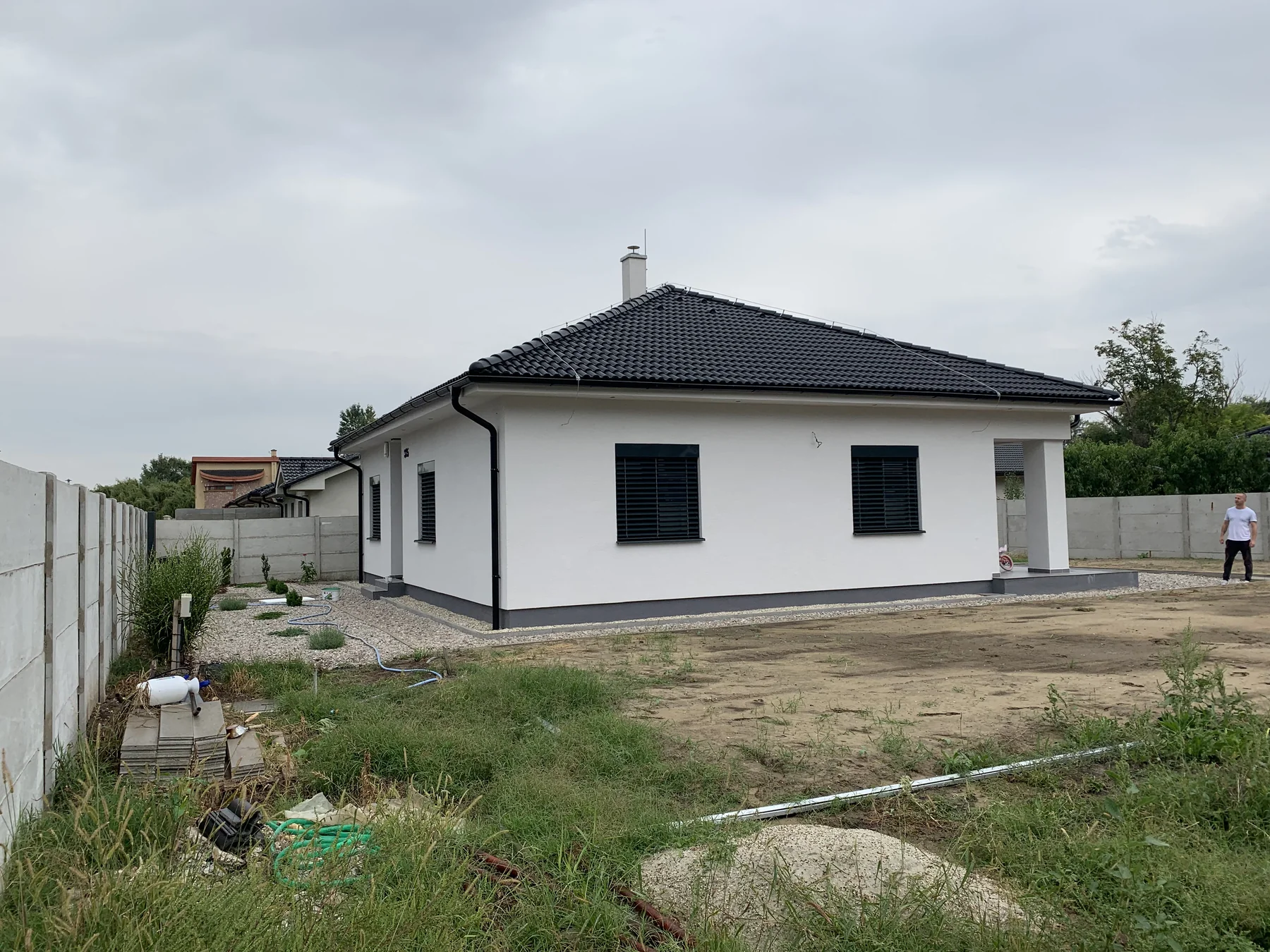 Biely rodinný dom s tmavou strechou a terénom pred domom