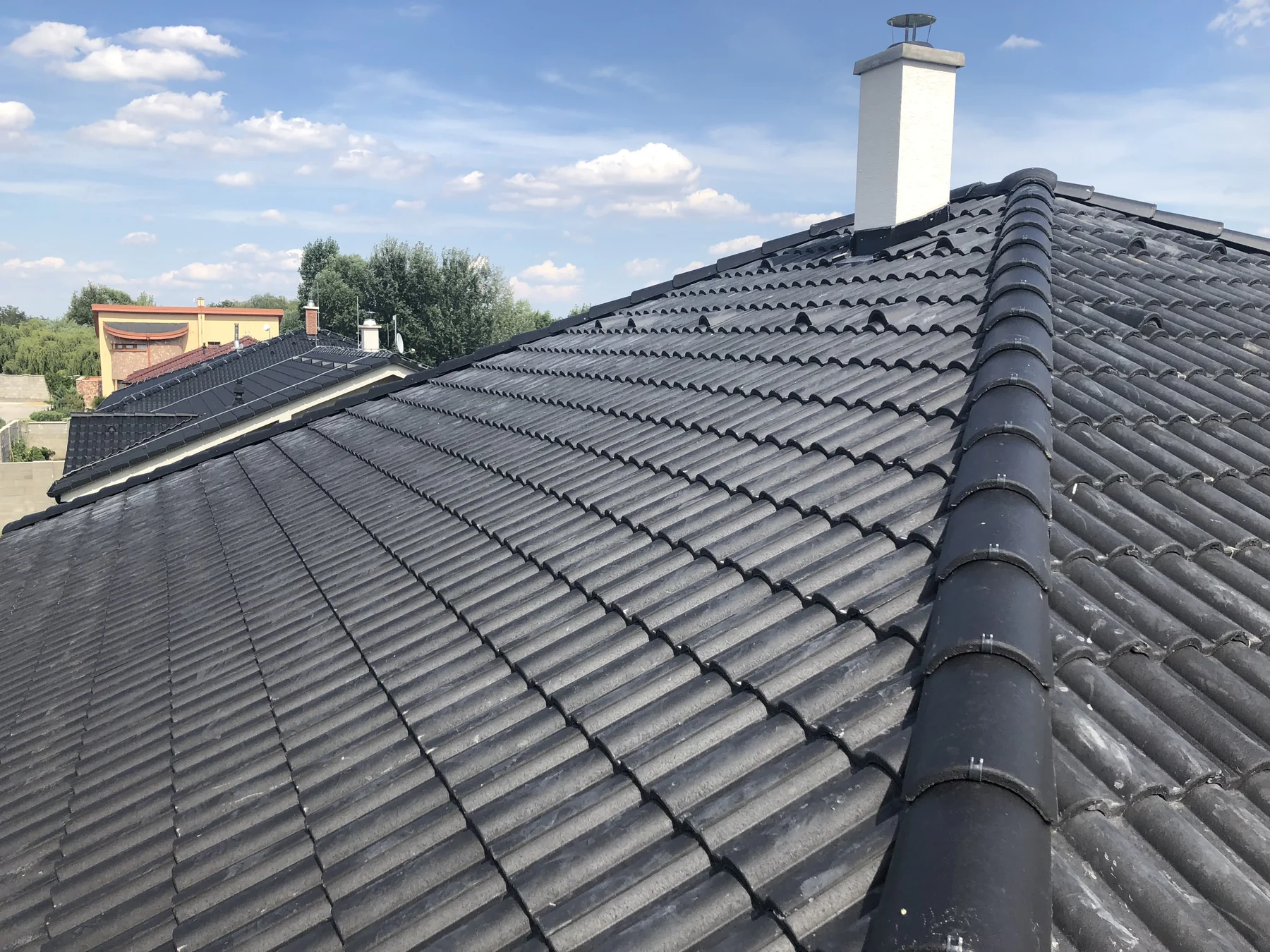 Detail tmavej strešnej krytiny s hrebeňom a komínom