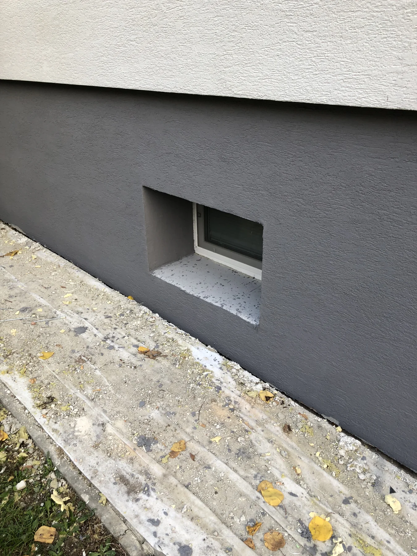 Detail sivého sokla, svetlej omietky a suterénneho okna